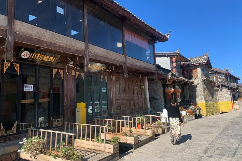 A woman walks past stores with "for rent" signs at a tourist attraction in Lijiang