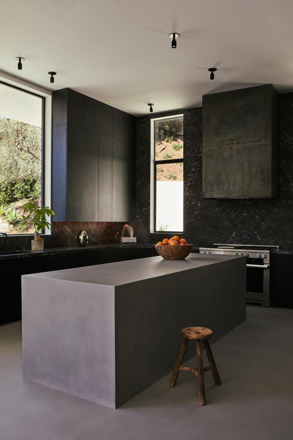 In the kitchen of a midcentury-inspired Hollywood Hills home designed by OSKLO, the blackened steel hood was custom-made, the countertops in honed negro d’Alba are from Stoneland, the spun fiber table lamp was purchased in Morocco, and the American Folk stool is from the 1930s. The knotted burl bowl on the custom concrete finished island was bought in Japan.