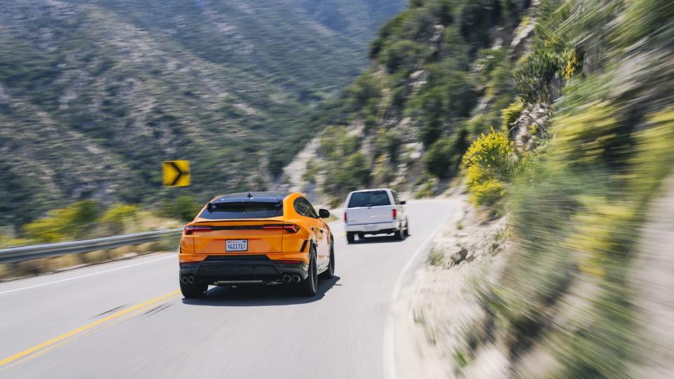 a couple of cars driving down a road with mountains in the background