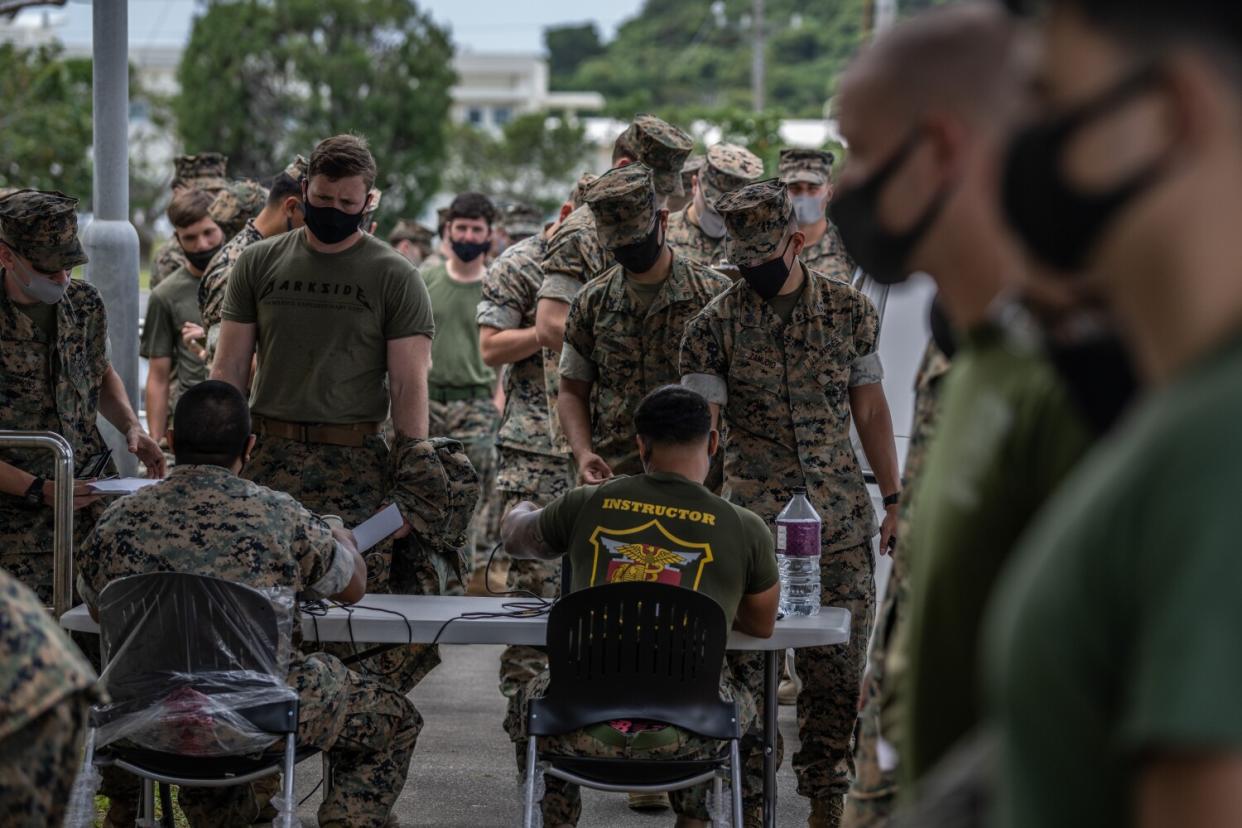 Two military members at a table face long lines of men in fatigues