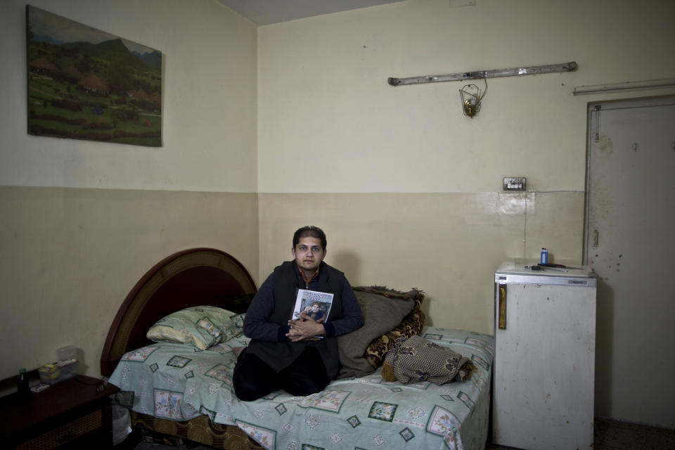 In this Wednesday, March 19, 2014 photo, Pakistani Doctor, Mohammed Amir, 31, son of Malik Sanaullah, 63, who was one of eleven victims killed by suicide bombers in an attack on a court complex on March 3, 2014, sits on his father's bed embracing his photograph, at their home in Islamabad, Pakistan. "I miss his guidance, I miss his advice, I will raise your head and make you proud," Amir said. (AP Photo/Muhammed Muheisen)