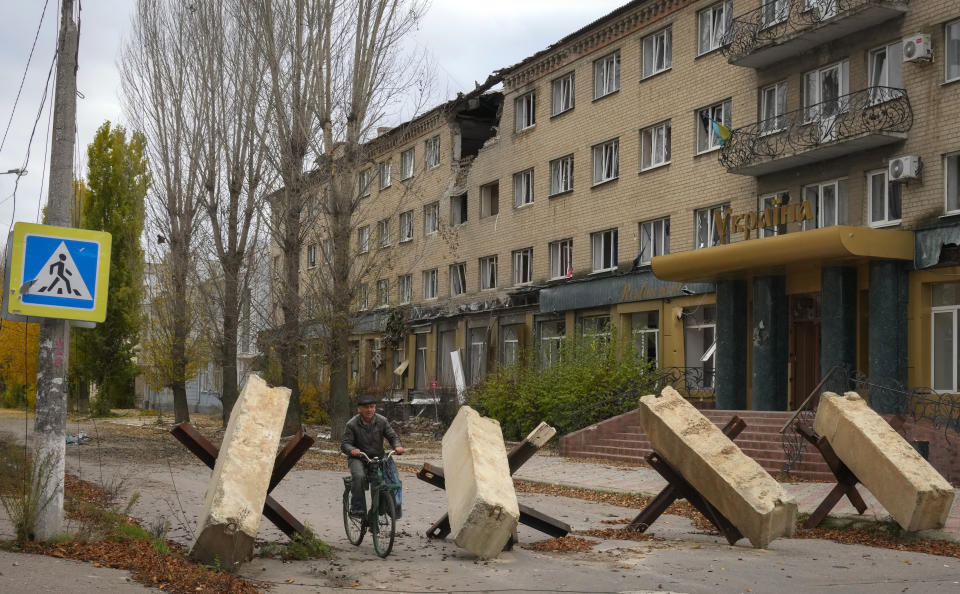 A man rides a bike past anti-tank hedgehogs, a city hotel in the background, in central Bakhmut, the site of the heaviest battle against the Russian troops in the Donetsk region, Ukraine, Friday, Oct. 28, 2022. (AP Photo/Efrem Lukatsky)