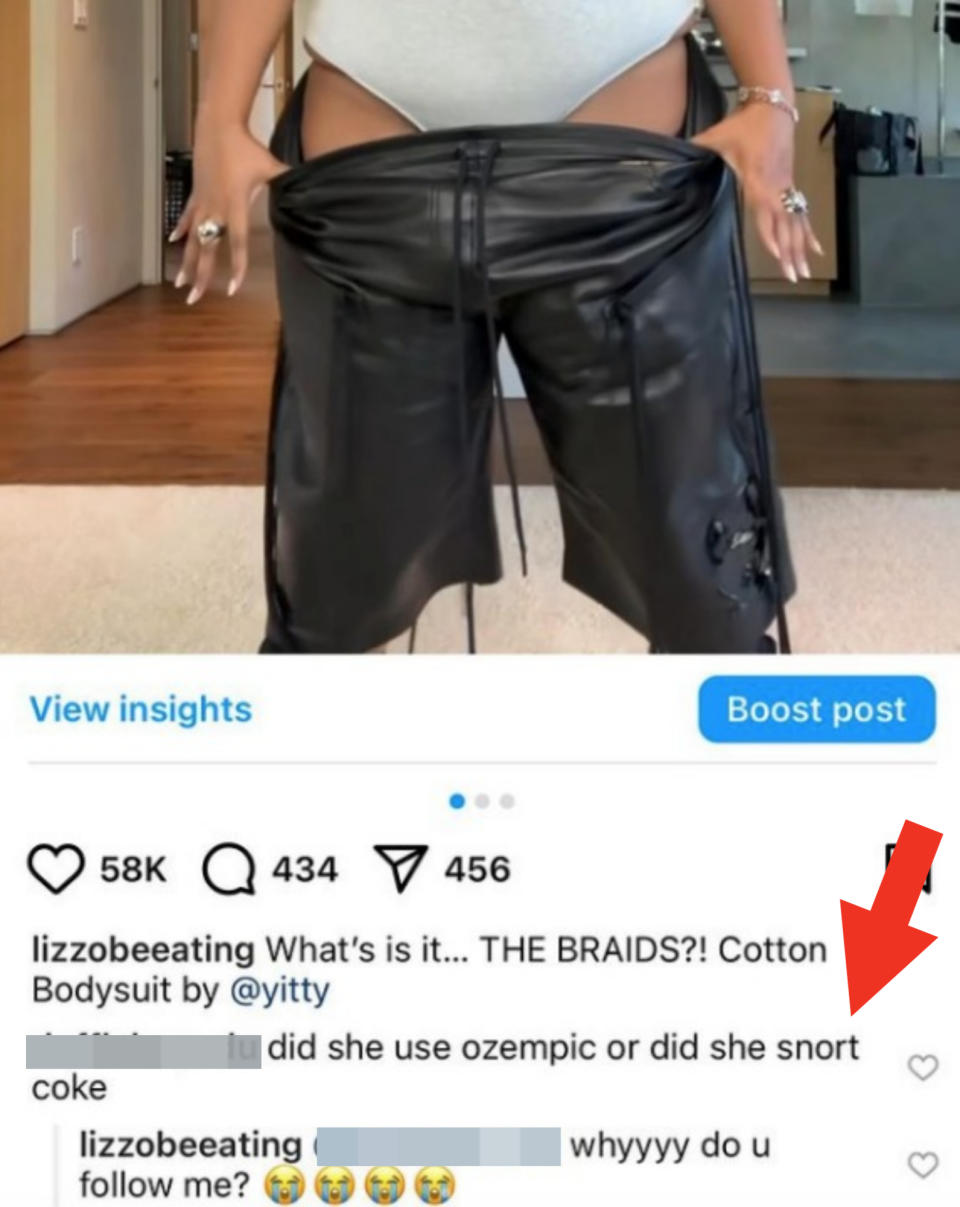 Lizzo wears a white cotton bodysuit by Yitty showing off black leather pants and holding up the waistband. Instagram post with caption and comments referring to her clothing and health