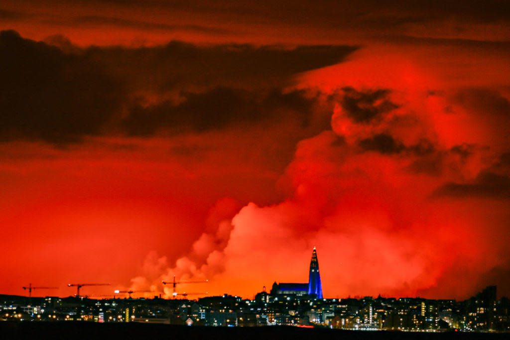 The skyline of Reykjavik is against the backdrop of orange-colored sky due to molten lava flowing out from a fissure on the Reykjanes peninsula north of the evacuated town of Grindavik, in western Iceland, on March 16, 2024.  / Credit: HALLDOR KOLBEINS/AFP via Getty Images