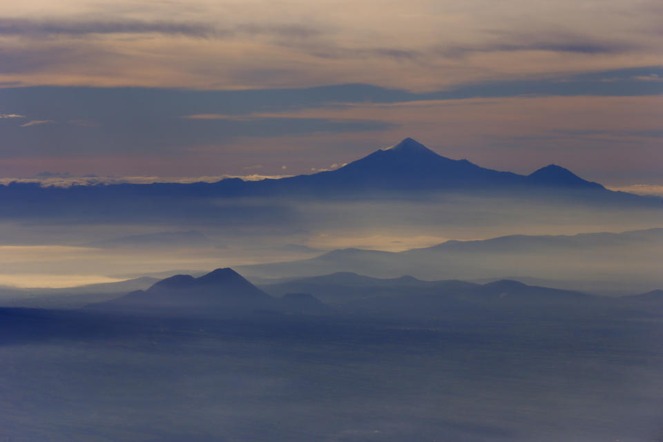 FILE - Mexico's highest peak and the third highest in North America, Pico de Orizaba, or Citlaltepetl mountain, which is a protected natural area, rises above the morning mist as seen from a Mexican Navy aircraft on a volcano monitoring mission in Mexico, July 23, 2013. Environmentalists say the administration of President Andrés Manuel López Obrador is trying to greenwash its legacy by adding dozens of new protected natural areas while simultaneously slashing funding for the environmental protection department. (AP Photo/Dario Lopez-Mills, File)
