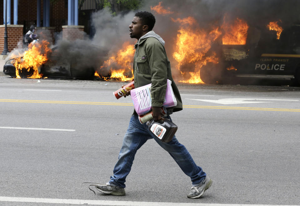 A man carries items from a store as police vehicles burn, Monday, April 27, 2015, after the funeral of Freddie Gray in Baltimore. Gray died from spinal injuries about a week after he was arrested and transported in a Baltimore Police Department van. (AP Photo/Patrick Semansky)