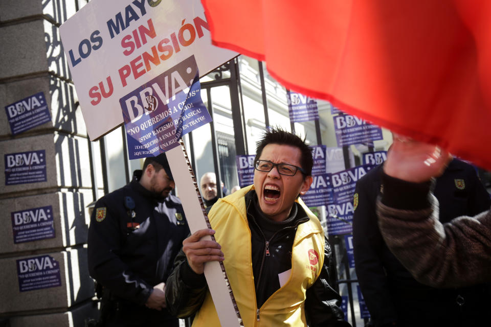 A man protests holding a banner reading in Spanish "The elder people without their pension" outside a BBVA bank building in Madrid, Spain, Friday, Feb. 15. 2019. Hundreds of Chinese have protested outside a Spanish bank's premises in Madrid, claiming they are being denied access to their accounts while the bank insists it is obeying money-laundering laws. (AP Photo/Andrea Comas)