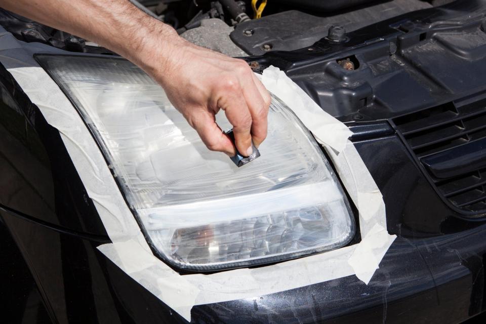 Hand applying headlight kit materials to a black car's headlight