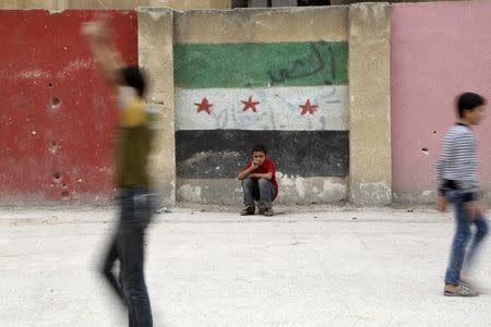 Boys play at a school's playground as one of them sits in front of a wall painted with an opposition flag in the rebel-controlled area of Aleppo's Seif al-Dawla, Syria October 25, 2015. REUTERS/Hosam Katan