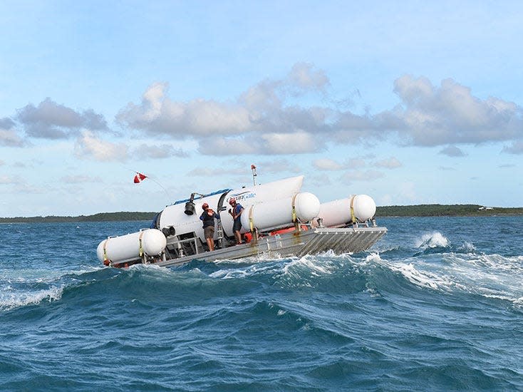 The Titan submersible on a floating platform with crew members, enroute to the dive location amidst rough waves.