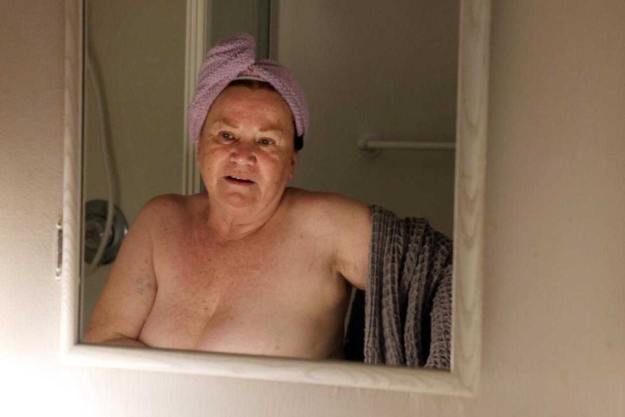 A woman with a towel on her head looks into a mirror