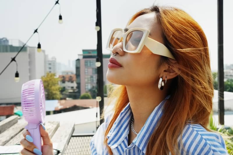 woman holding a portable electric mini fan near her face while sitting at rooftop cafe