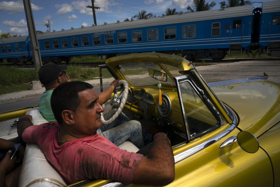 A passenger in an American classic car watches as the first train using new equipment from China rides past, in Havana, Cuba, Saturday, July 13, 2019. The first train using new equipment from China pulled out of Havana Saturday, hauling passengers on the start of a 915-kilometer (516-mile) journey to the eastern end of the island as the government tries to overhaul the country’s aging and decrepit rail system. (AP Photo/Ramon Espinosa)