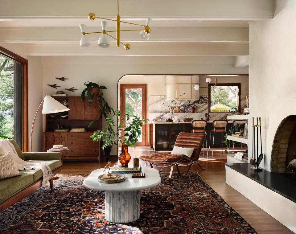 In the home’s living room, rounded built-in shelves coated in plaster were added to either side of the existing fireplace. Walnut trim emphasizes the arched opening leading into the kitchen.