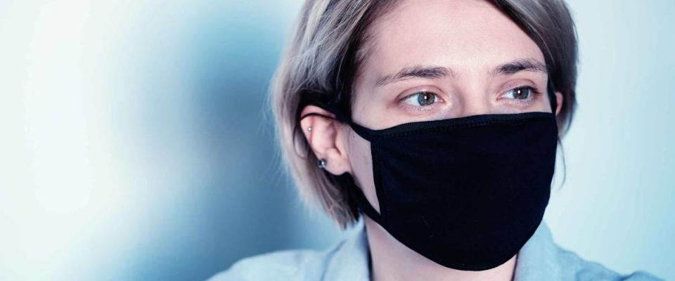 Portrait of a sad woman in a black mask on a white wall in isolation during a pandemic - virus corona covid 19