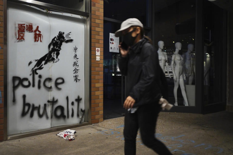 A protester walks past graffiti depicting police as a dog and various slogans including "Hongkongers Resist, "Chinese Communist whole family die" at the Hong Kong Polytechnic University in Hong Kong on Wednesday, Nov. 20, 2019. A small band of anti-government protesters, their numbers diminished by surrenders and failed escape attempts, remained holed up at a Hong Kong university early Wednesday as they braced for the endgame in a police siege of the campus. (AP Photo/Vincent Yu)