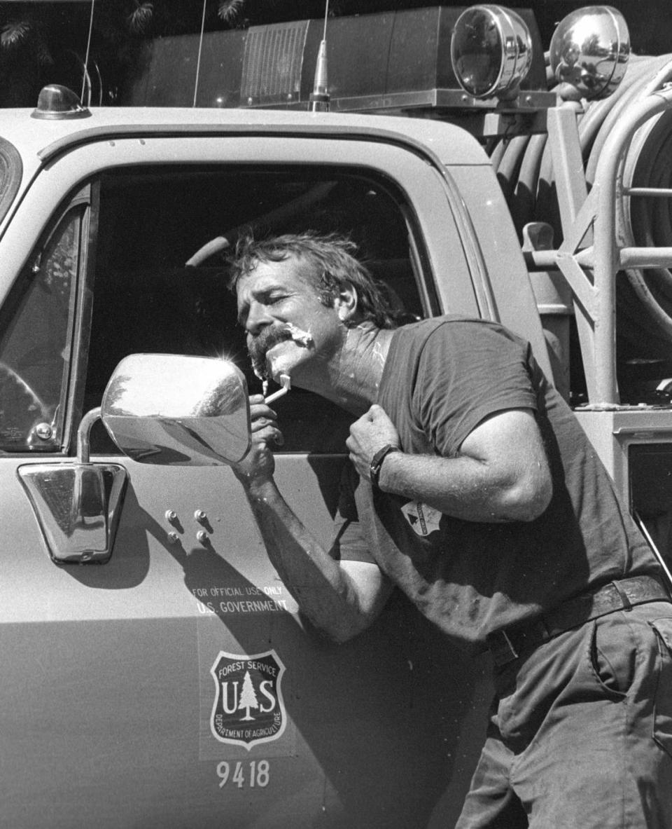 Firefighter Mark Linane of U.S. Forest Service shaves using his truck side mirror after taking a four-hour rest period while fighting the Hi Mountain Fire on July 7, 1988.