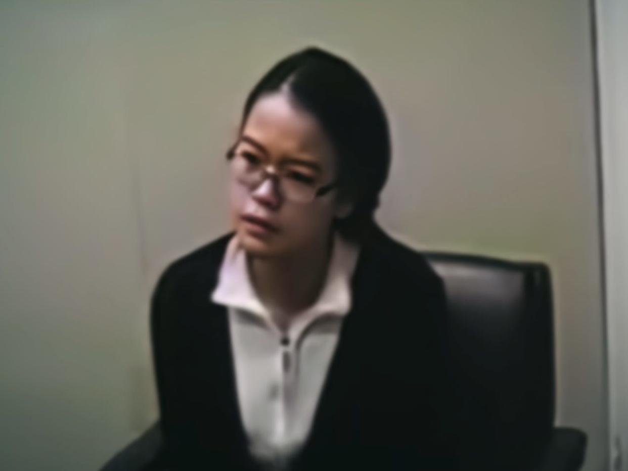 jennifer pan, a young woman with black hair and  glasses, sitting in a chair wearing a white shirt and black cardigan. the image quality is grainy and she looks inquisitve