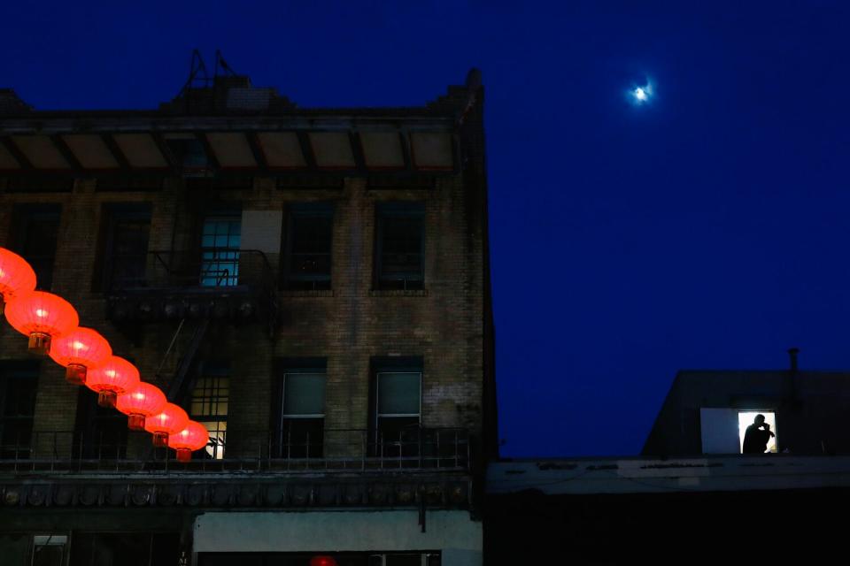 Red lanterns glow above a street; higher up, a dot of moon shines.