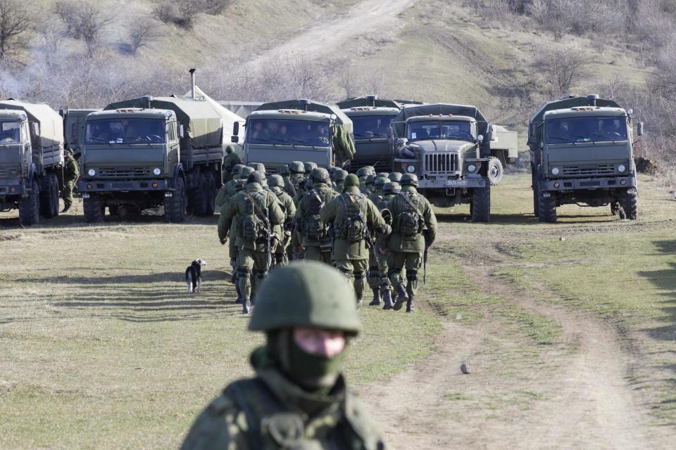 Military personnel, believed to be Russian servicemen, walk outside the territory of an Ukrainian military unit in the village of Perevalnoye outside Simferopol