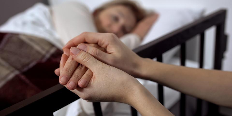 A person holding another terminally ill patient's hand, comforting them.