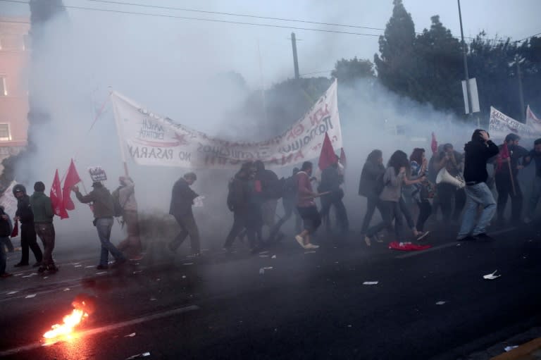 Protesters run for cover as tear gas canisters explode during clashes with riot police during a demonstration in Athens on May 8, 2016