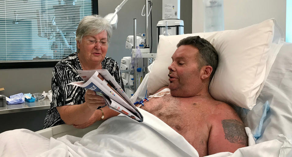 Buddy’s mother, Clare Miller, reads the newspaper to him in hospital. Ms Miller has left the hospital only for the odd shower and trip to her local church to pray for her son. Image: Supplied