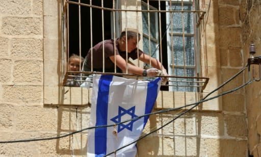 An Israeli settler places an Israeli flag on the window of a Palestinian house after it was occupied by settlers near the Ibrahimi Mosque, or the Tomb of the Patriarch, in the West Bank city of Hebron on March 27, 2018