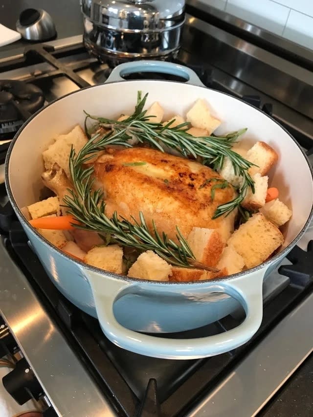 Roasted chicken in a Dutch oven with bread cubes, vegetables, and fresh herbs