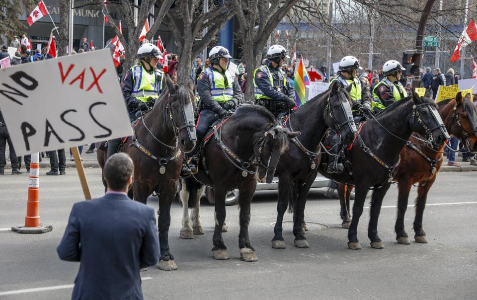 Police officers on horseback keep watch as hundreds of demonstrators gather at city hall in Calgary, Alta., in March 2022 to protest COVID-19 vaccine mandates. THE CANADIAN PRESS/Jeff McIntosh