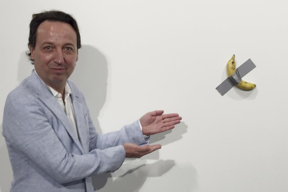 FILE- In this Dec. 4, 2019 photo, gallery owner Emmanuel Perrotin poses next to Italian artist Maurizio Cattlelan's "Comedian" at the Art Basel exhibition in Miami Beach, Fla. The work sold for $120,000. A Miami couple who bought a headline-grabbing banana duct-taped to a wall say they acknowledge the absurdity of the artwork, but believe it will become an icon and plan to gift it to a museum. (Siobhan Morrissey via AP)
