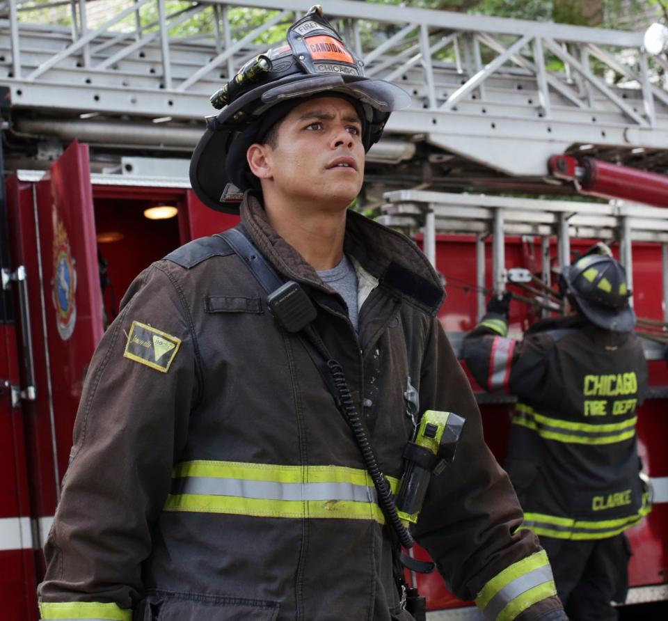 Charlie Barnett dressed in firefighter gear in front of a firetruck and other firefighters getting set up