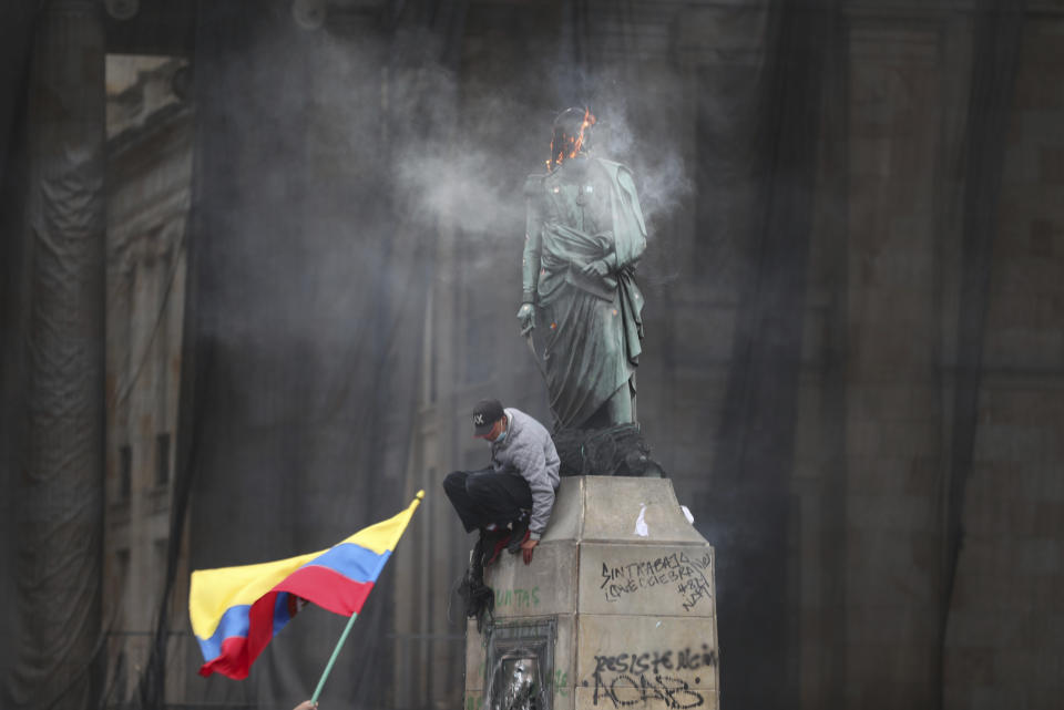 Un manifestante baja de una estatua del héroe independentista Simón Bolívar después de prender fuego a una malla protectora en su cabeza, durante una marcha contra el gobierno en la Plaza Bolívar en Bogotá, Colombia, el miércoles 12 de mayo de 2021. (AP Foto/Fernando Vergara)