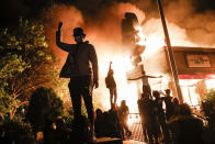 In this image released by World Press Photo, Thursday April 15, 2021, by John Minchillo, Associated Press, part of a series titled Minneapolis Unrest: The George Floyd Aftermath, which won third prize in the Spot News Stories category, shows Protesters raise their fists in defiance outside a burning fast-food restaurant near the precinct station of the officers who arrested Floyd, in Minneapolis, Minnesota, USA, on May 29, 2020. (John Minchillo, Associated Press, World Press Photo via AP)