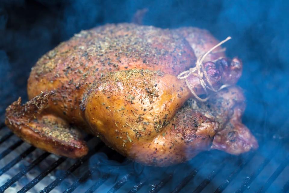 Spiced rubbed chicken being grilled in a smoker barbeque.
