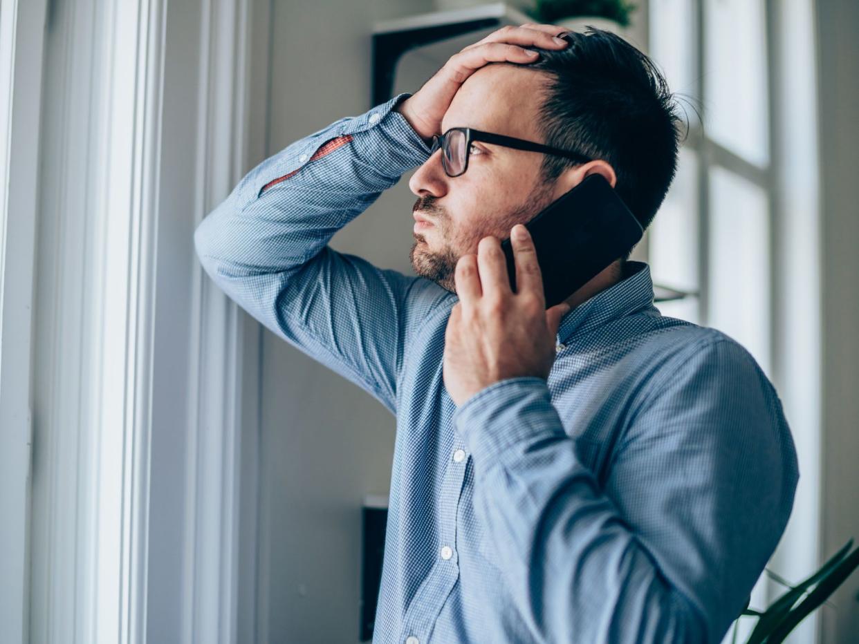 Worried businessman with hand on forehead talking on mobile phone in his office.