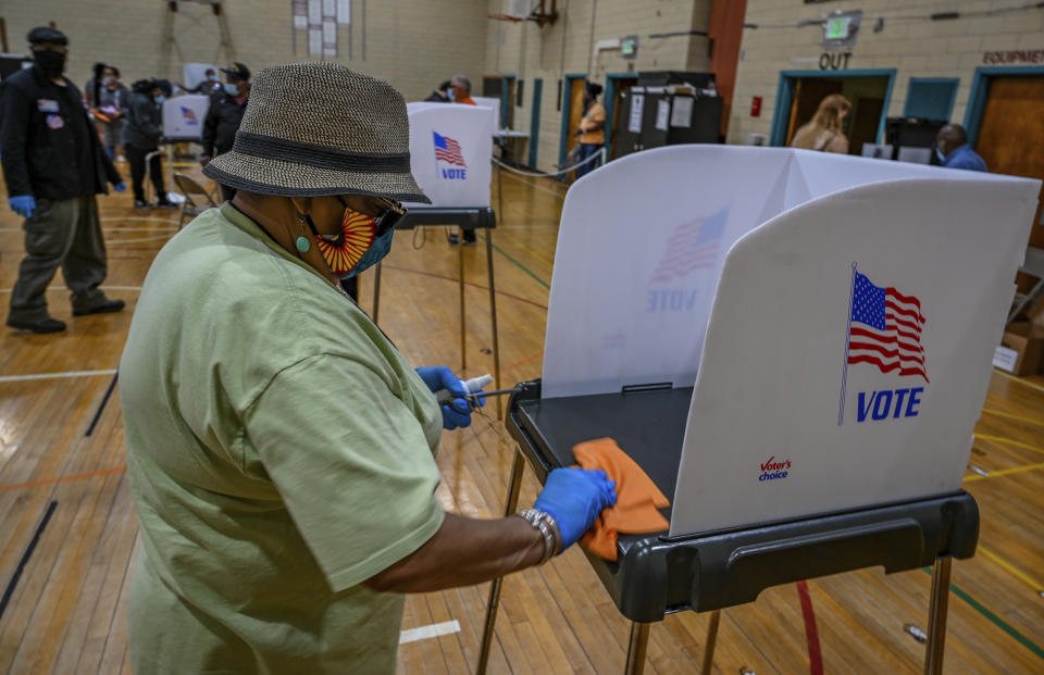 Election tech Veda Tucker sanitizes a voting booth between voters during the primary election in Baltimore, Tuesday, June 2, 2020. (Jerry Jackson/The Baltimore Sun via AP)