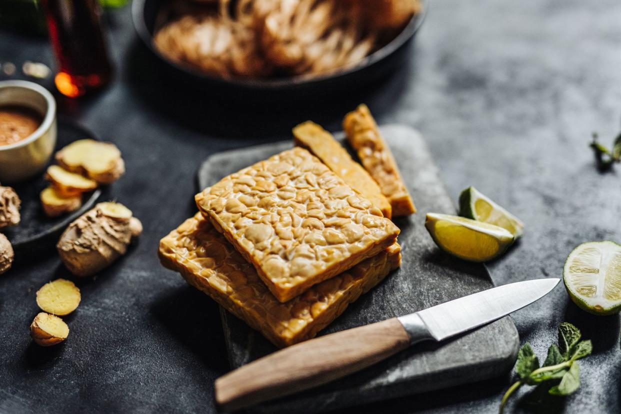 close up of tempeh on cutting board with kitchen knife with other ingredients on table preparing a vegan dish in kitchen