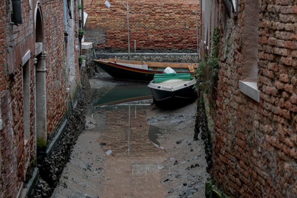 Boats are docked along a dried canal during a low tide in Venice, Italy, Tuesday, Feb. 21, 2023. Some of Venice's secondary canals have practically dried up lately due a prolonged spell of low tides linked to a lingering high-pressure weather system.