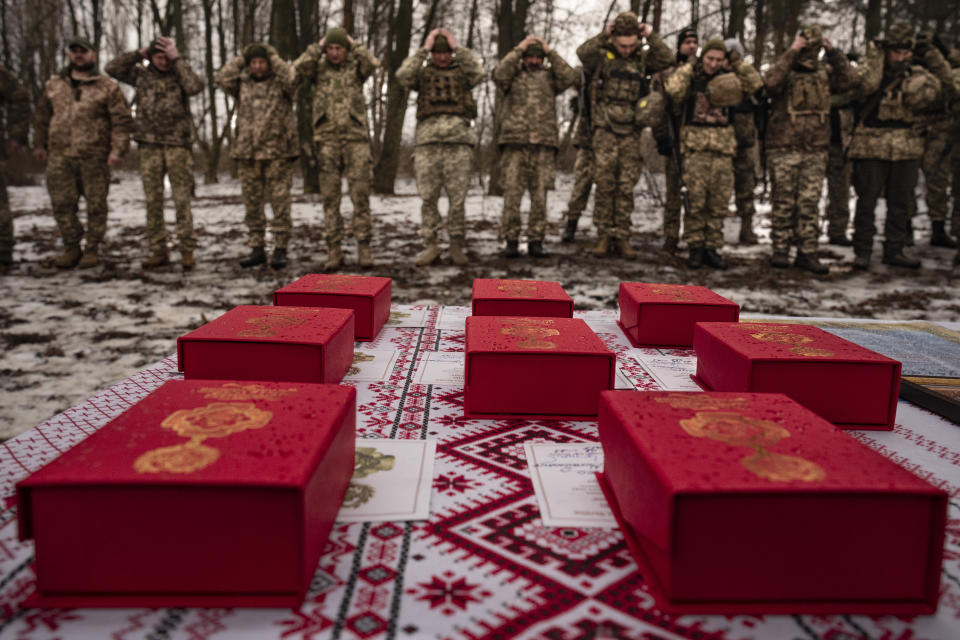 Medals are placed on a table as Ukrainian servicemen of the Prince Roman the Great 14th Separate Mechanized Brigade adjust their hats before a flag ceremony where some of them were honored for their bravery and accomplishments in battle, in the Kharkiv area, Ukraine, Saturday, Feb. 25, 2023. (AP Photo/Vadim Ghirda)