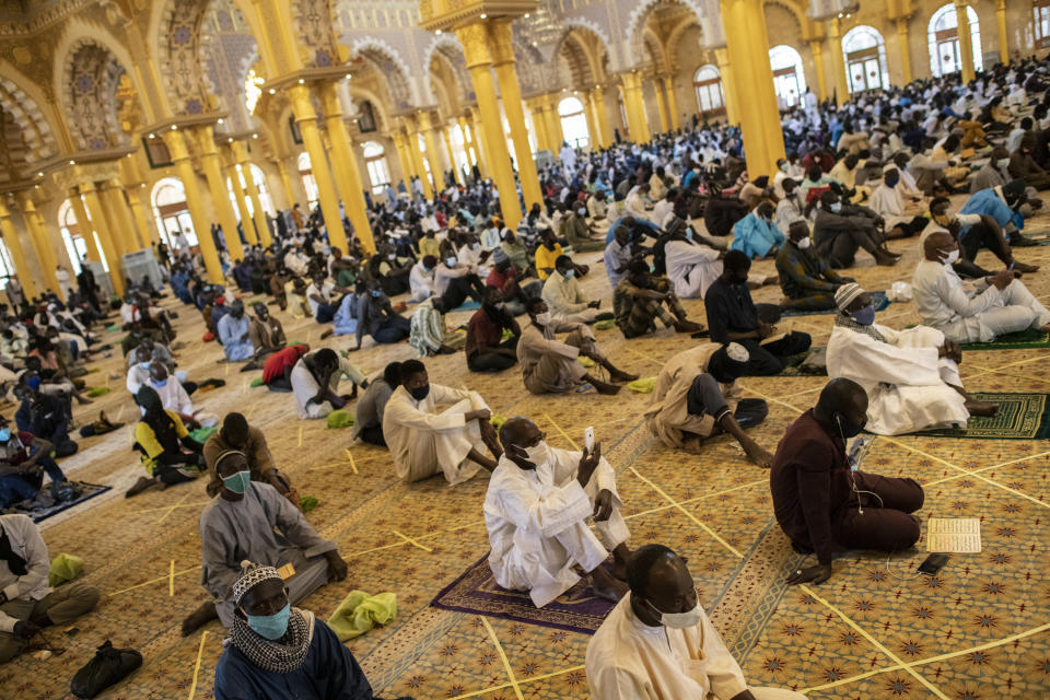 In this photo taken Friday, May 15, 2020, a follower of the Senegalese Mouride brotherhood, an order of Sufi Islam, films with his smartphone as he and others practice social distancing as they attend Muslim Friday prayers at West Africa's largest mosque the Massalikul Jinaan, in Dakar, Senegal. A growing number of mosques are reopening across West Africa even as confirmed coronavirus cases soar, as governments find it increasingly difficult to keep them closed during the holy month of Ramadan. (AP Photo/Sylvain Cherkaoui)