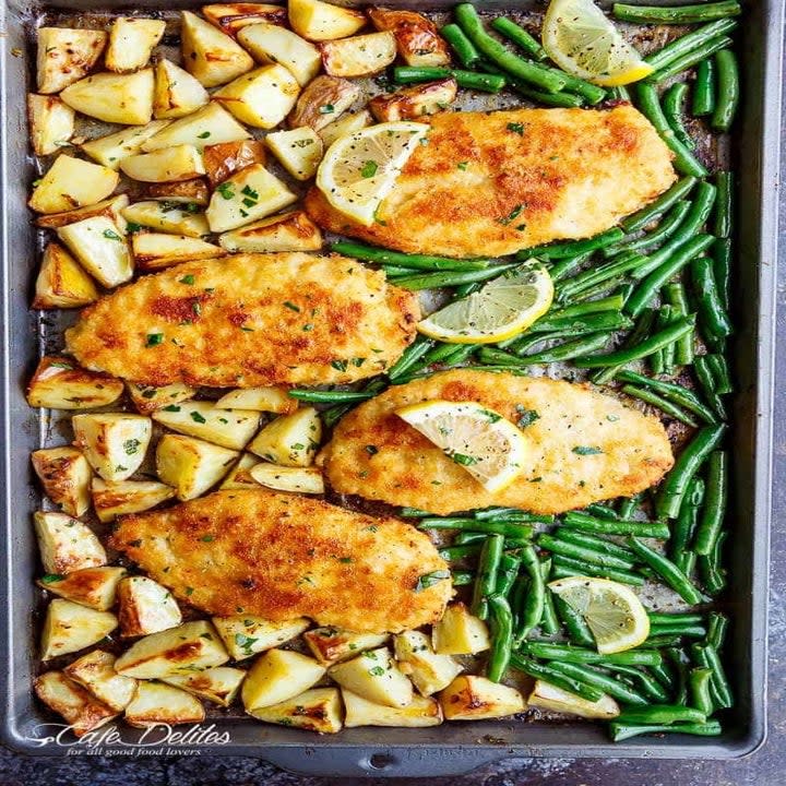 Crispy chicken cutlets surrounded by potato wedges and green beans on a sheet pan