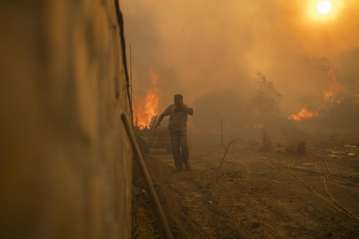 A local runs to avoid the flames of a wildfire in Gennadi village, on the Aegean Sea island of Rhodes, southeastern Greece, on Tuesday, July 25, 2023. A firefighting plane has crashed in southern Greece, killing both crew members, as authorities are battling fires across the country amid a return of heat wave temperatures. (AP Photo/Petros Giannakouris)