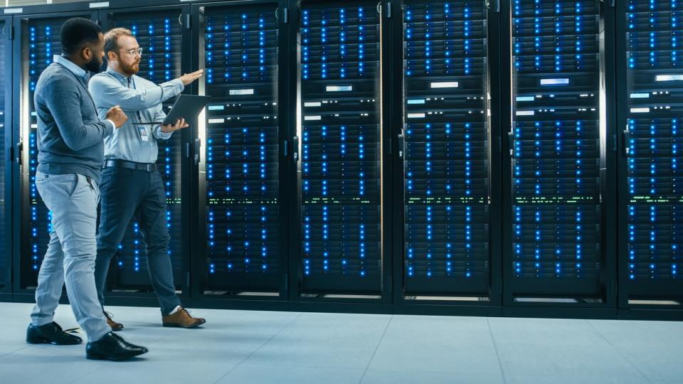 Two people talk while walking past servers in a data center.