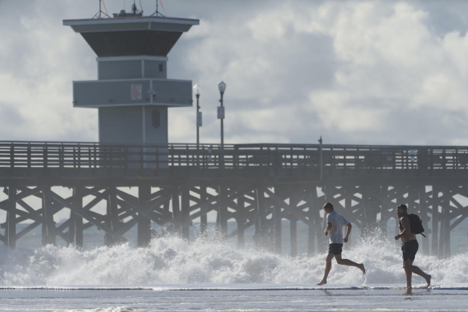 People run on the edge of the flooded beach next to the pier in Seal Beach, Calif., Saturday, Dec. 30, 2023. (AP Photo/Damian Dovarganes)