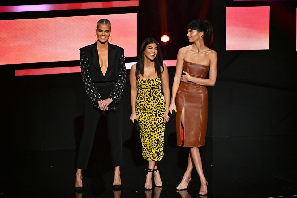 Khloe, Kourtney in a strapless yellow and cheetah print midi dress and Kendall on stage.