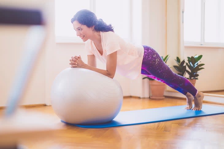 woman doing a stir-the-pot plank with forearms on a stability ball, one of the best exercises for preventing back pain