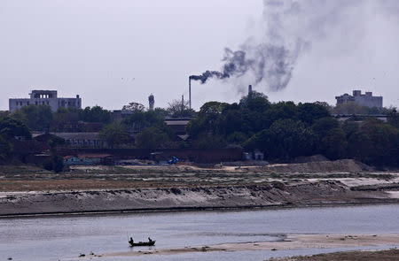 Men row a boat in the river Ganges as smoke emits from a chimney of a leather tannery at an industrial area in Kanpur, India, May 4, 2018. Picture taken May 4, 2018. REUTERS/Adnan Abidi