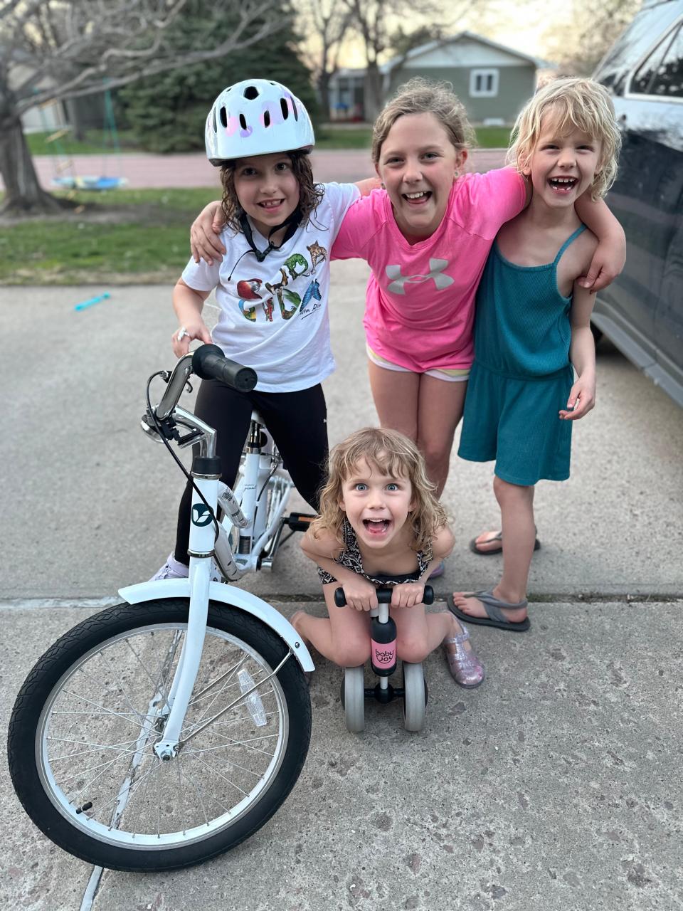 Four young girls smiling outside on bicycles.