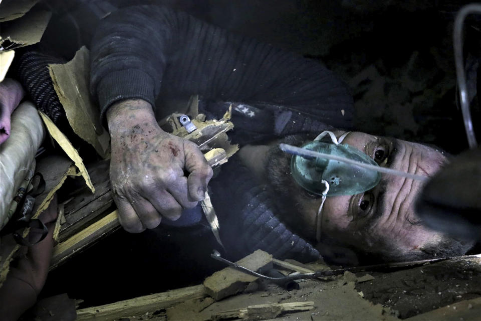 In this photo provided by the Syrian Civil Defense White Helmets, which has been authenticated based on its contents and other AP reporting, a man lies under debris of a collapsed building on the southern edge of the city of Idlib, Syria, Wednesday, Feb. 9, 2022. The White Helmets said Thursday the building collapsed in northwest Syria leaving a woman and three of her children dead while her husband and three other children were pulled out alive. (Syrian Civil Defense White Helmets via AP)